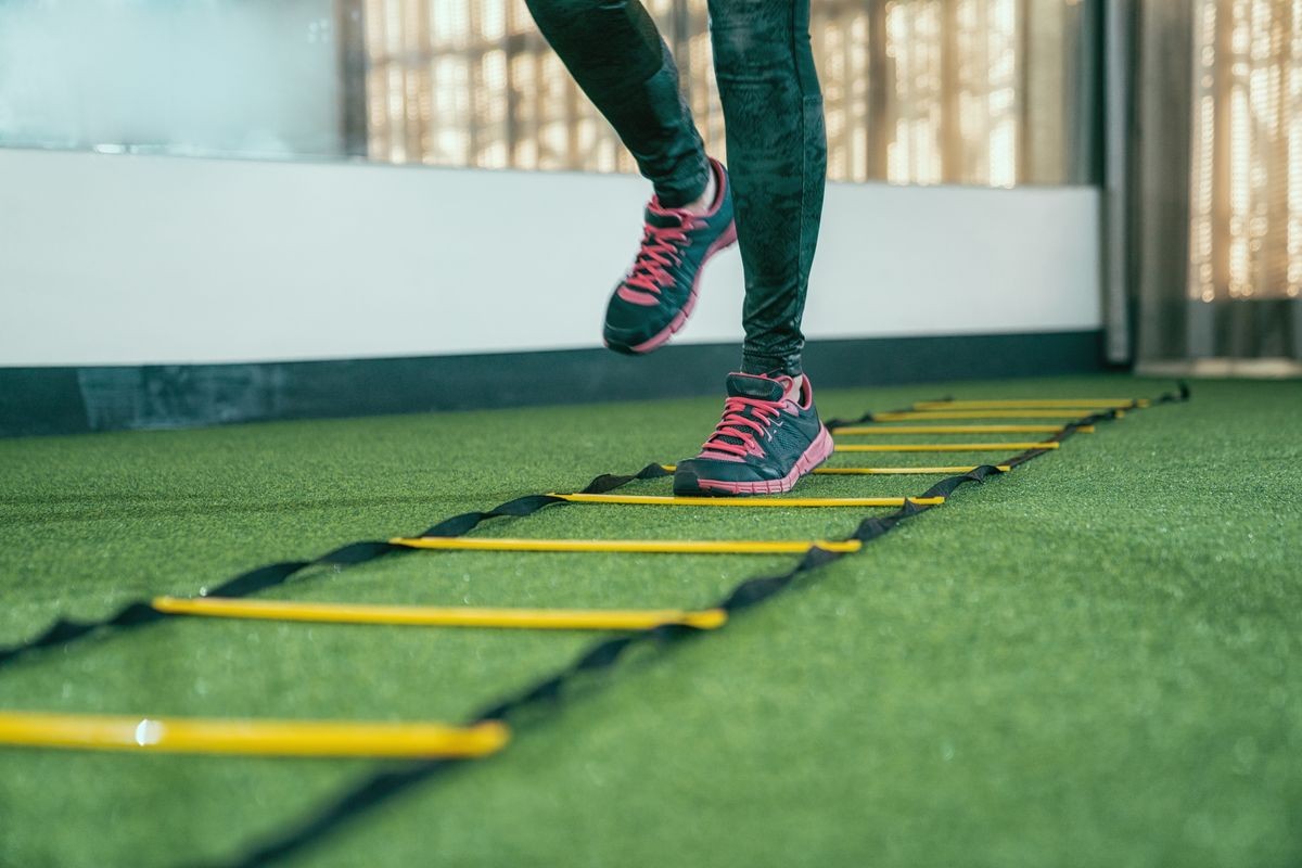 unrecognized female athlete practicing for hurdle running race in gym. focus on legs with sneakers doing workout run faster quicker in a health club. people love sports exercise lifestyle concept.